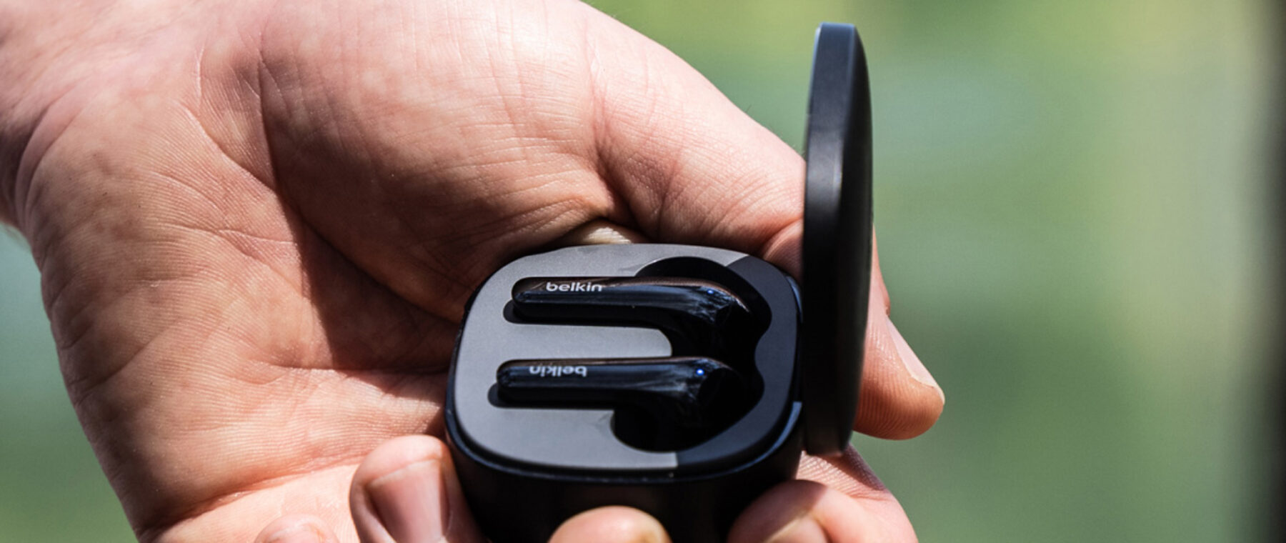 A man holds a case containing a set of Belkin ear buds